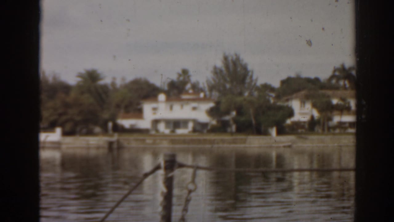 Waterfront houses and trees seen across calm water through dark vertical framing.