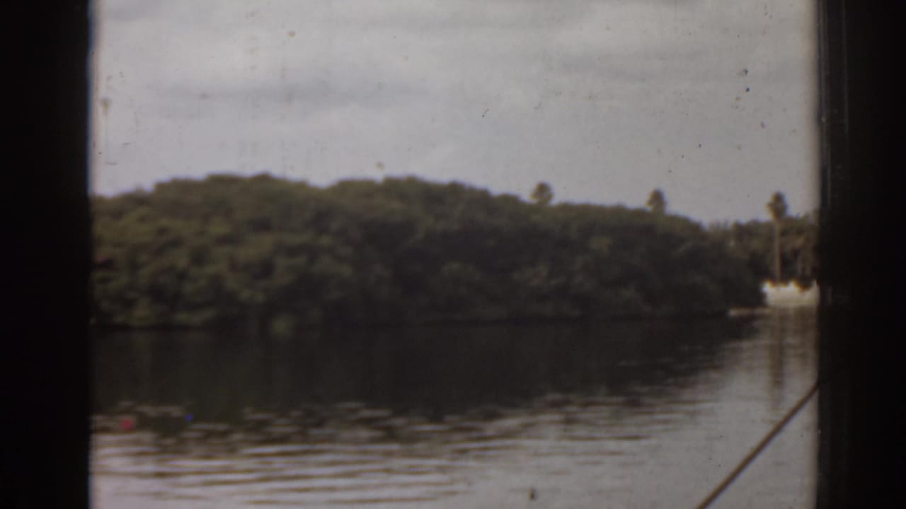 Boat-window view across calm water toward a wooded island under an overcast sky.