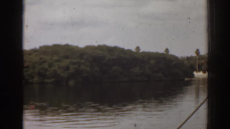 1963 Florida 8mm view from a boat window, looking across still water toward a tree-covered island with dark frame edges.