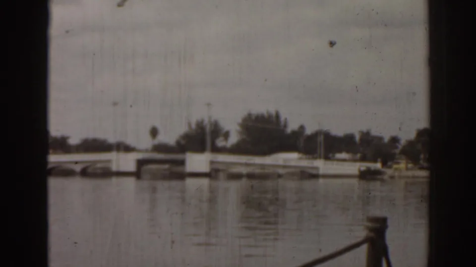 1963 Florida 8mm view from a boat toward a low white bridge, still water, and distant trees.