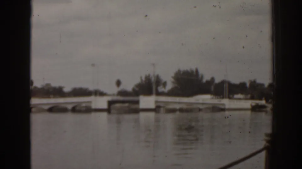 1963 Florida home-movie frame showing a low bridge across the water from a moving boat perspective.