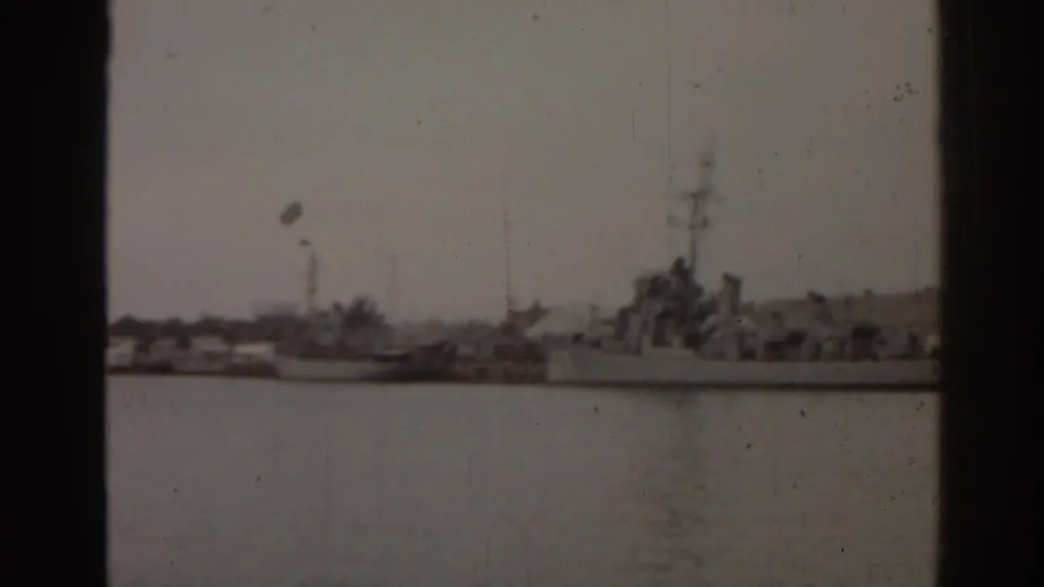 Soft 8mm frame from 1963 Florida showing a naval-looking vessel moored near boats and low waterfront structures.