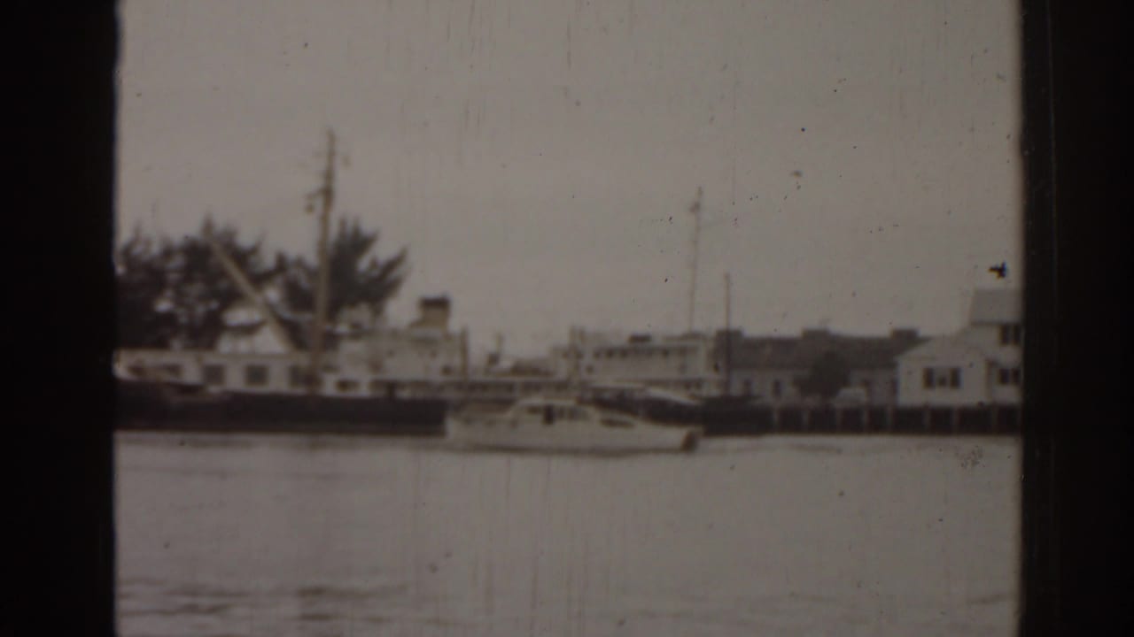 1963 Florida home-movie frame showing a harbor with small boats, waterfront buildings, water, and visible 8mm gate borders.
