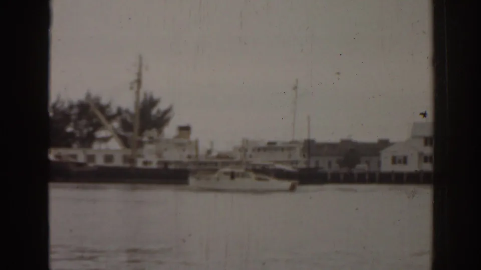 1963 Florida home-movie frame showing a harbor with small boats, waterfront buildings, water, and visible 8mm gate borders.
