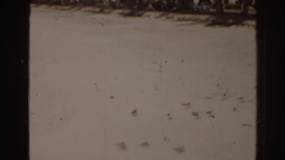 A soft, scratched 8mm frame shows pale sky, dust, and small distant marks within the Florida beach scene.