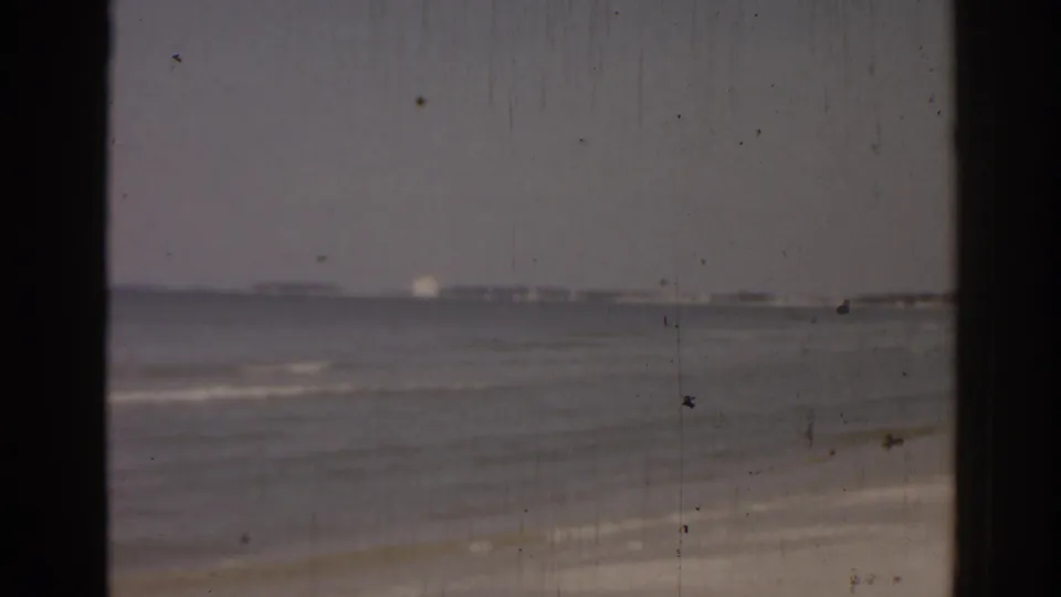 1963 Florida 8mm footage shows gentle surf beside a sandy beach, with a distant horizon and visible film grain and scratches.