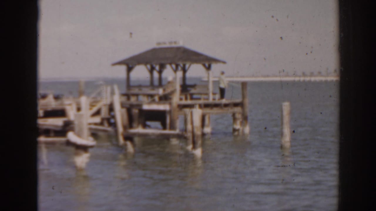 Roofed wooden dock over calm water with a distant shoreline behind it.