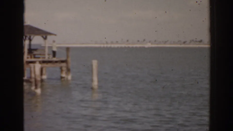 1963 Florida 8mm frame with the roofed dock partly cropped, a single piling, open water, and distant shore.