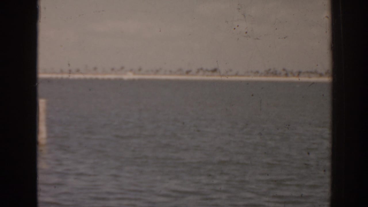 Calm lake water with a distant low shoreline seen through dark film edges.
