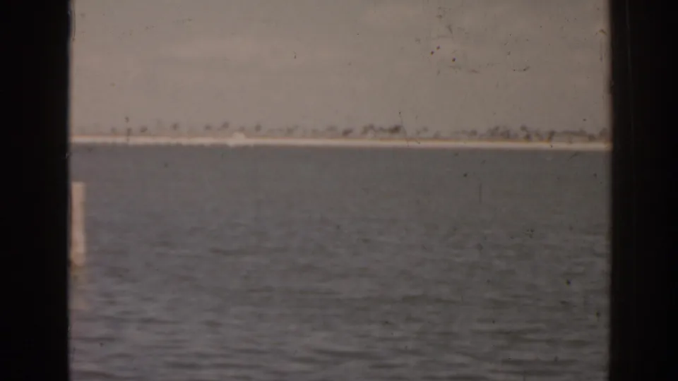 1963 Florida home-movie frame showing rippled lake water and a faint distant shoreline under a muted sky.