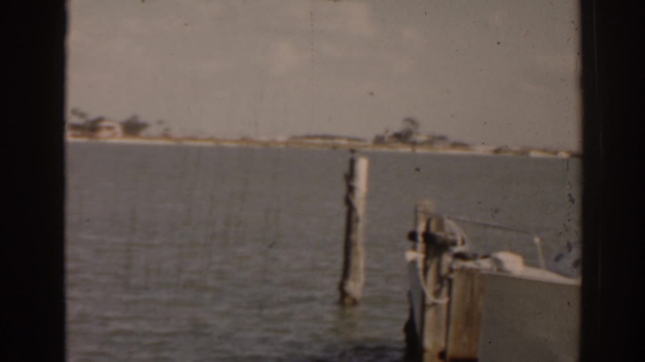 Soft 8mm view of calm water, dock pilings, and the bow of a moored boat.