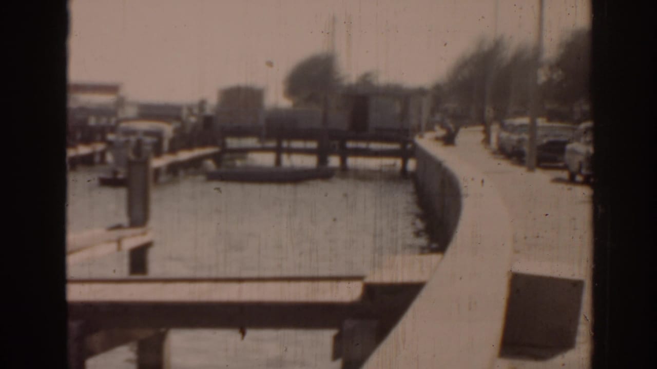 Canal with wooden docks and parked cars along a sunny street.