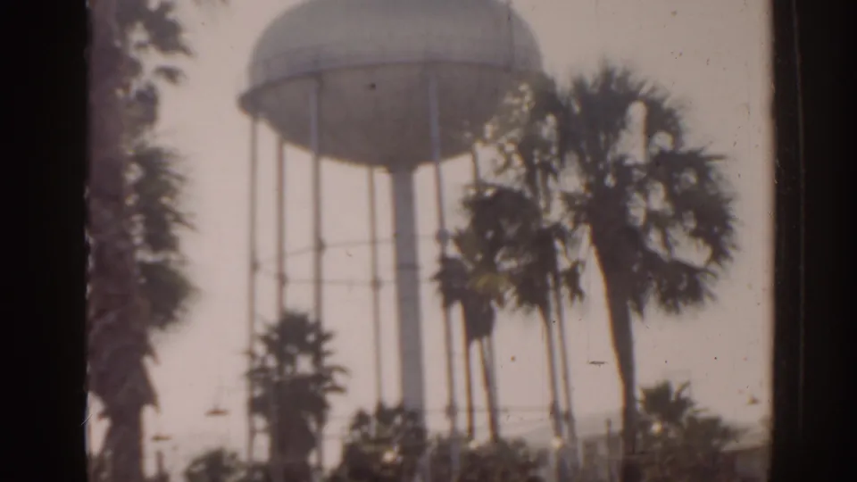 1963 Florida 8mm frame showing an elevated water tower partly obscured by palm trees and soft film exposure.