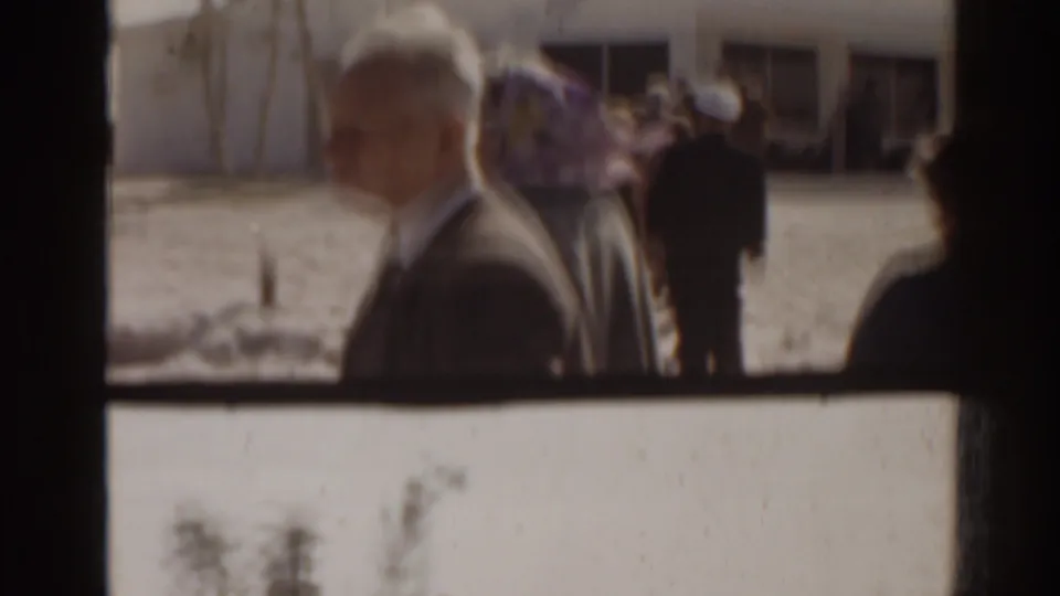 1963 Florida frame showing adults in line or gathered near a white marina building, seen through soft 8mm focus.