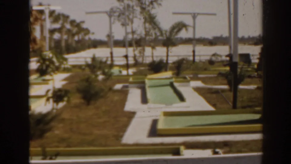 A final 1963 Florida view of the mini-golf course shows geometric pastel greens, white walkways, palms, and clipped grass in bright sun.