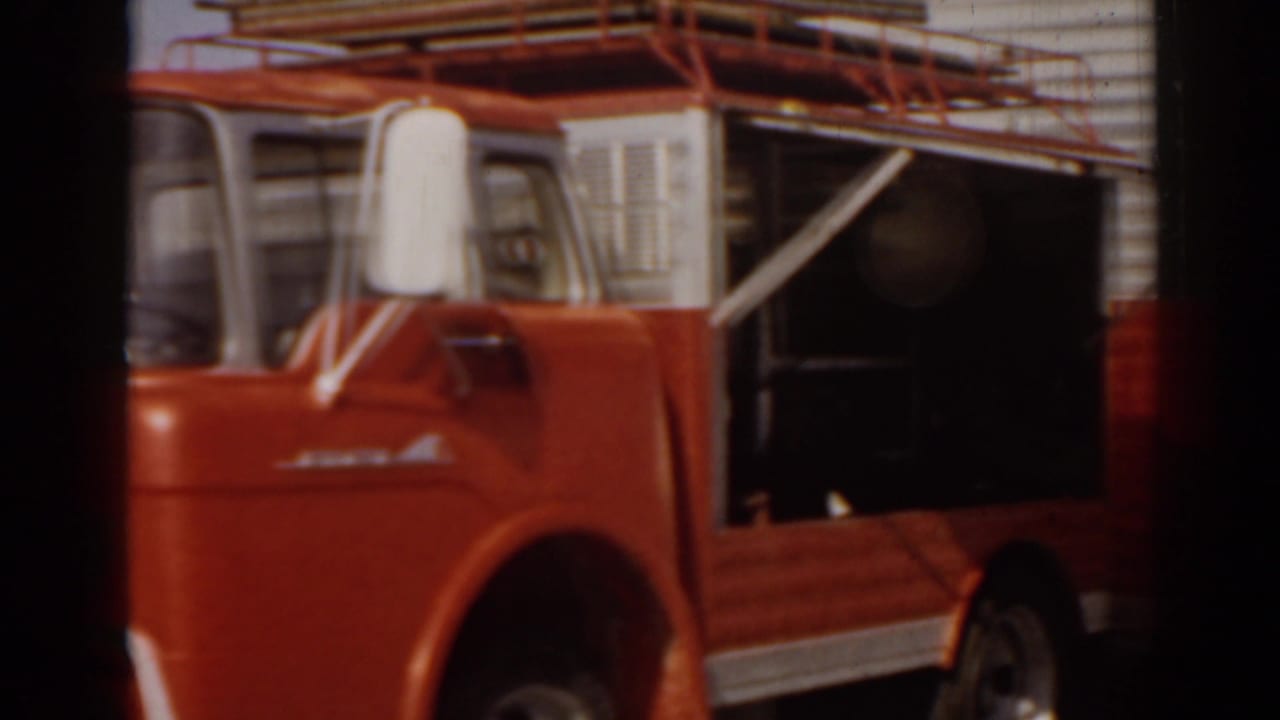 Red and white food truck with side compartment and roof rack in bright sun.