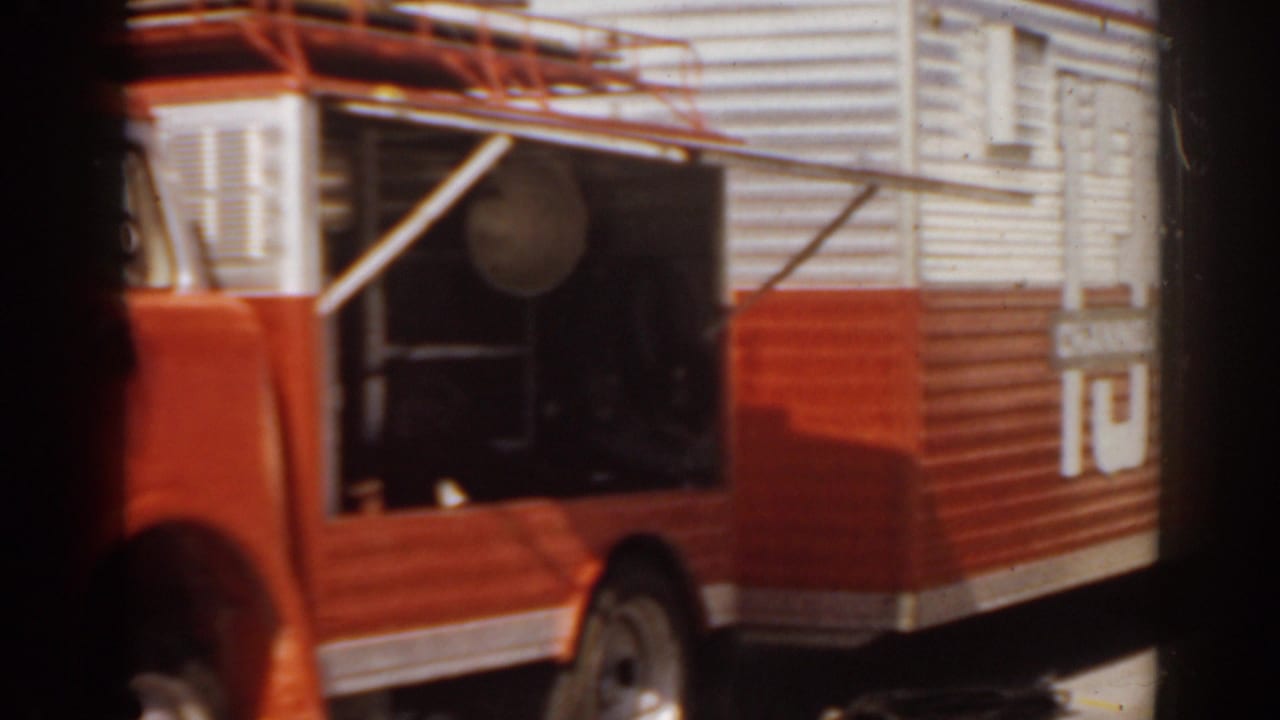 Side of a red and white truck with open compartment and circular vent.