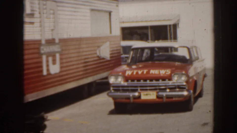 1963 Florida 8mm frame showing a red and white WTVT News car parked near the corrugated food truck in bright daylight.