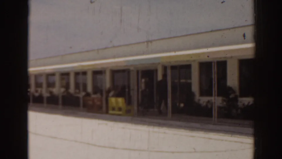 1963 Florida 8mm frame showing a building exterior with a shaded walkway, entrance area, and sunlit pavement.