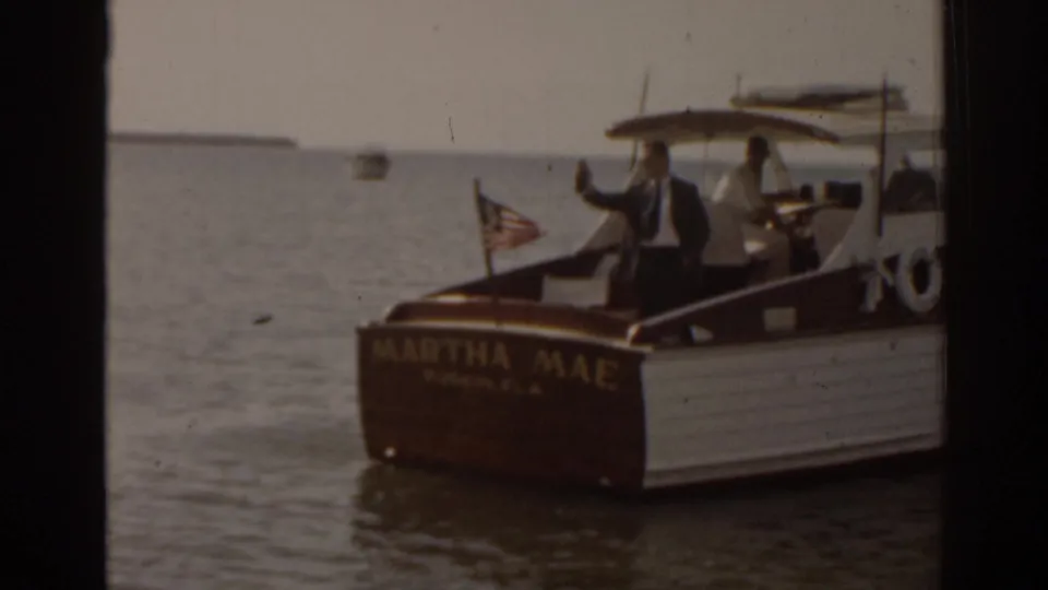 A suited passenger waves from the stern of the MARTHA MAE, a wooden cruiser on Florida water in supported 1963 8mm footage.