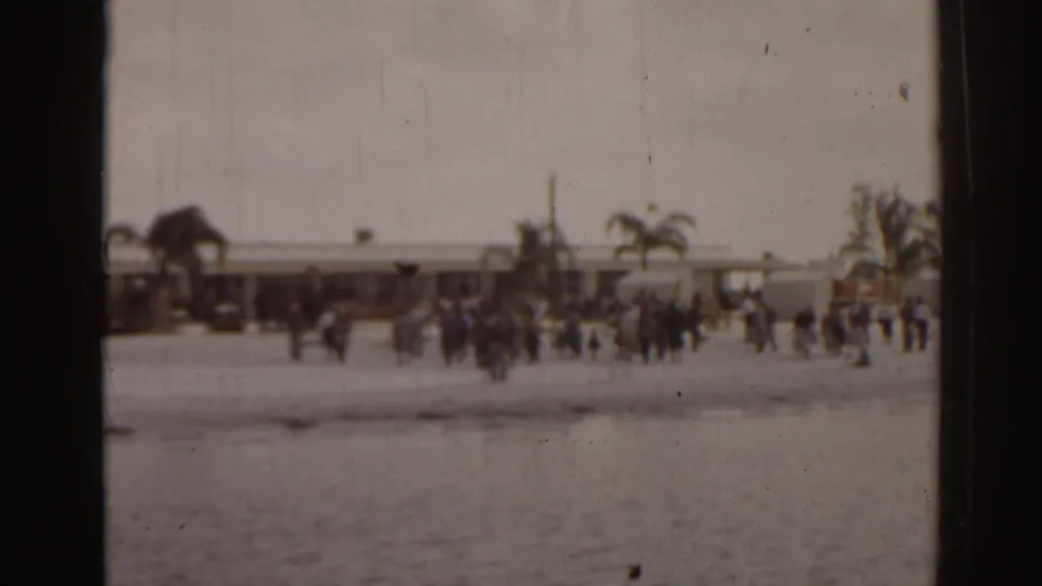 1963 Florida waterfront view with people gathered along a beach or pier area, seen softly across the water on 8mm film.