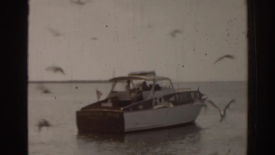 1963 Florida 8mm frame of the Martha Mae seen from behind on open water, with gulls crossing the foreground and horizon beyond.