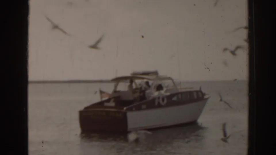 1963 Florida home-movie frame showing a small motorboat on the water with birds crossing the soft 8mm frame.
