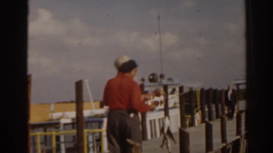 1963 Florida 8mm frame showing a man from behind on a dock, with railings, posts, water, and a cloudy sky.