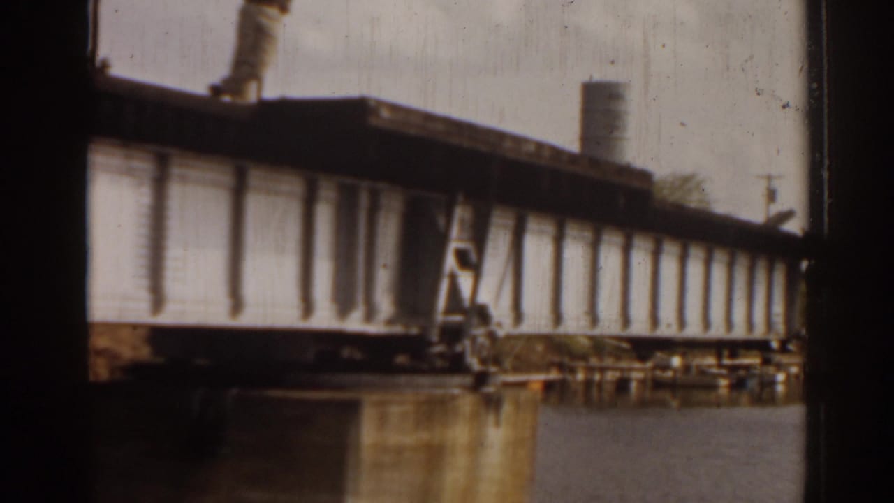 1963 Florida 8mm frame showing a raised drawbridge section over still river water, with shoreline buildings and trees in the background.