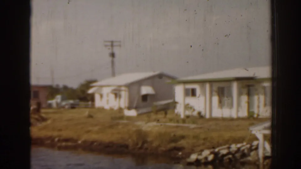 1963 Florida neighborhood view showing a modest single-story house, open lawn, utility pole, and river foreground.