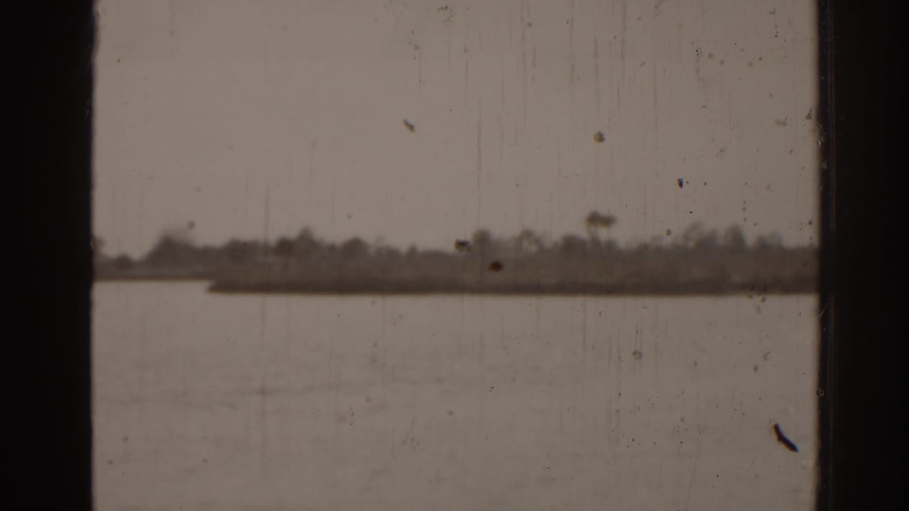Water and a distant low shoreline seen through a dark vertical window frame.