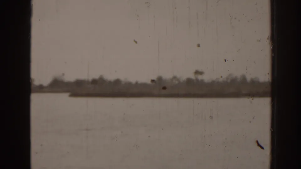 1963 Florida 8mm view across a calm body of water toward a low tree-lined shore, divided by a dark window frame.