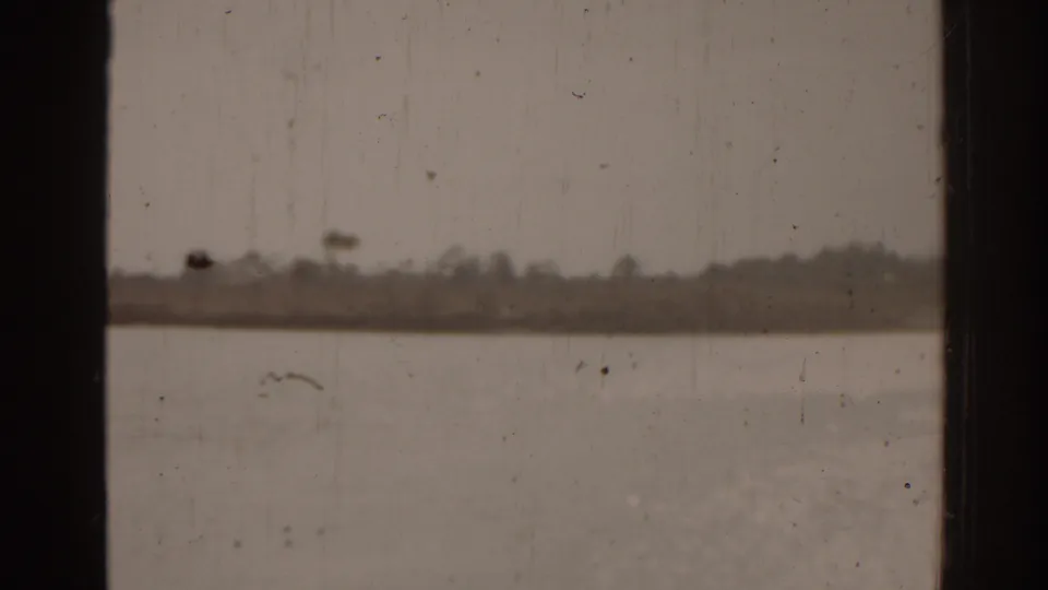 1963 Florida 8mm frame showing water, a low distant shore, and a dark window edge with visible dust and scratches.