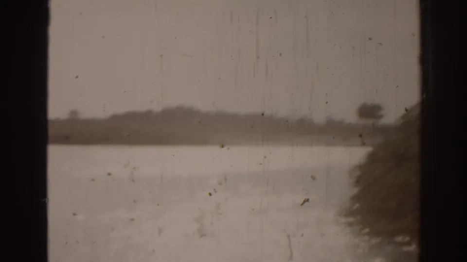 1963 Florida 8mm view through a window toward water and distant trees, with shoreline vegetation entering at the right edge.