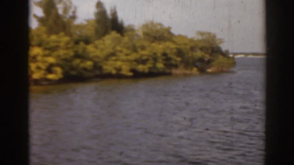 1963 Florida home-movie frame showing the end of a green island with open coastal water beyond it.