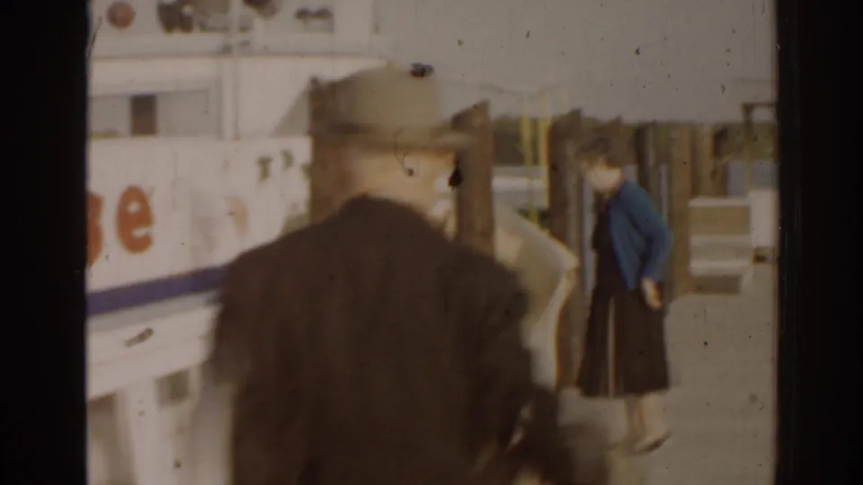 1963 Florida home-movie frame showing visitors near a docked Jungle Cruise boat, partially obscured by posts and soft focus.