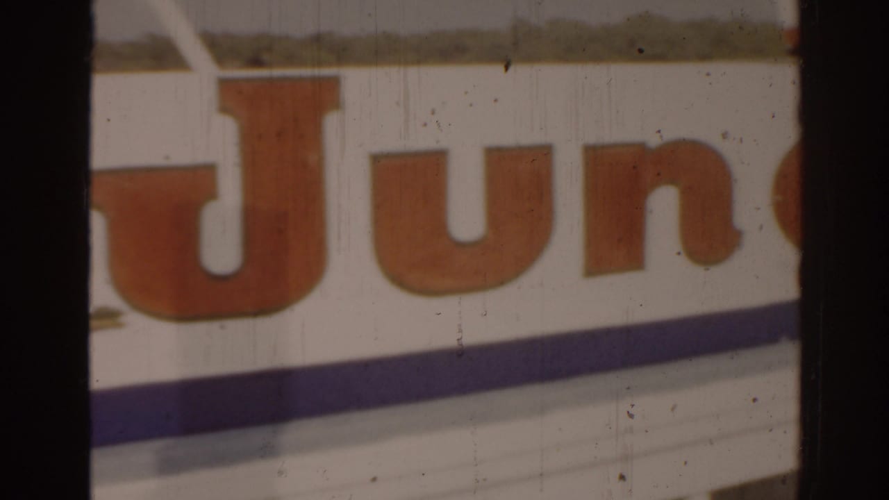 Partial train or vehicle sign with large orange letters beside a street scene.