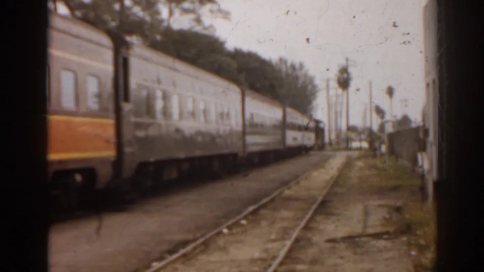 1963 Florida 8mm view of passenger train cars moving along rail tracks, filmed from a moving vehicle or adjacent trackside position.
