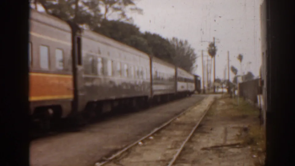 1963 Florida home-movie view of passenger train cars along adjacent tracks, seen from a moving vehicle with palm trees nearby.