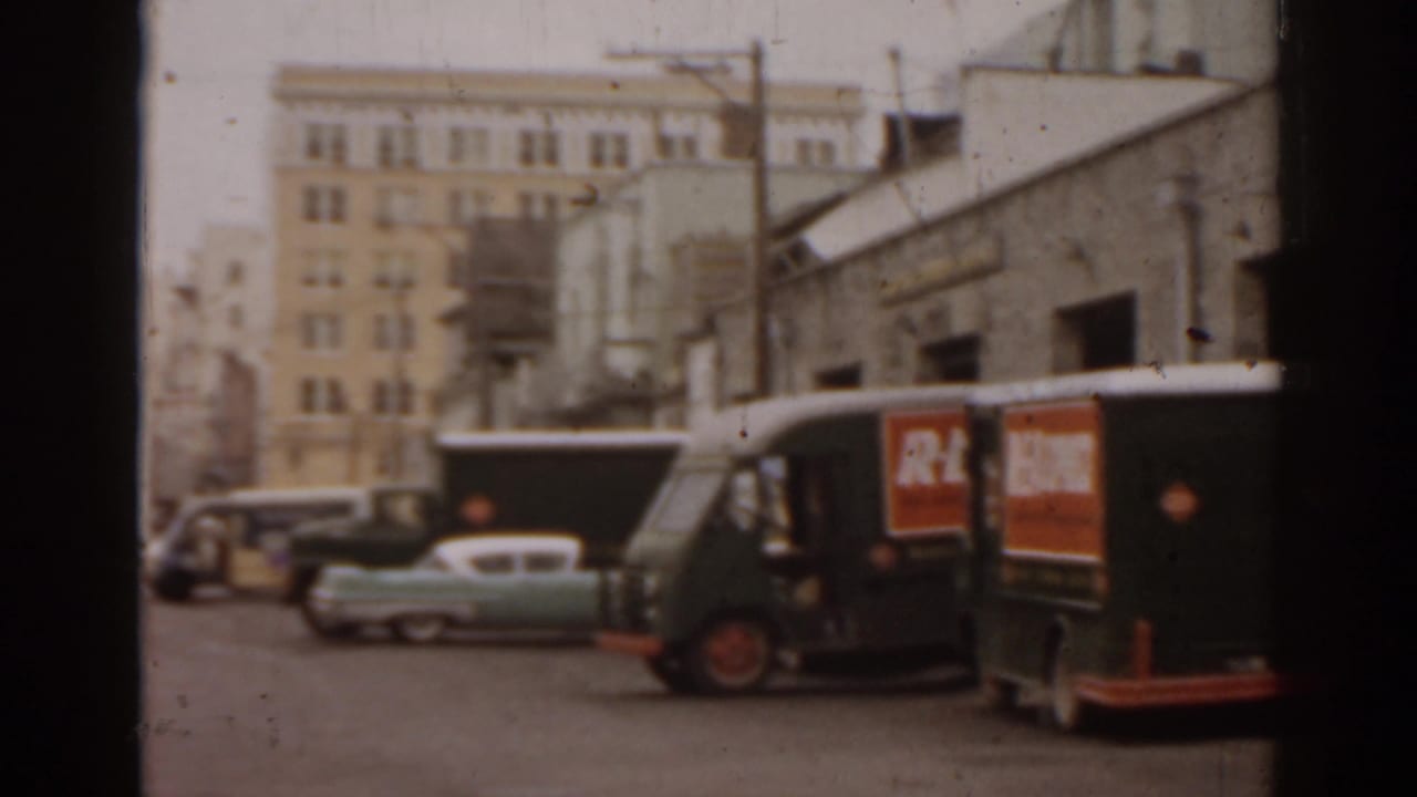 Street scene with parked cars, a delivery truck, utility poles, and multi-story buildings.