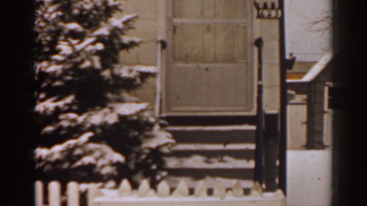 Snow-covered porch steps, picket fence, and evergreen beside a residential exterior.