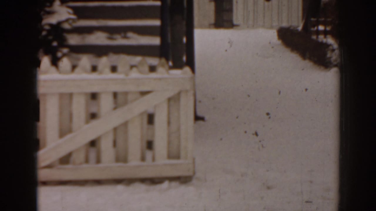 1963 Florida frame with snow on a residential porch railing, steps, and adjacent wall in soft 8mm focus.