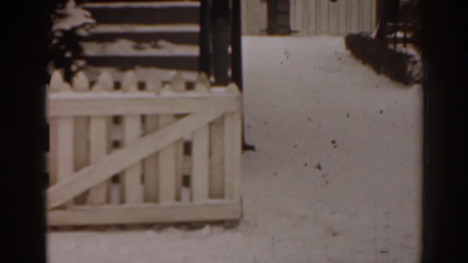 1963 Florida frame with snow on a residential porch railing, steps, and adjacent wall in soft 8mm focus.