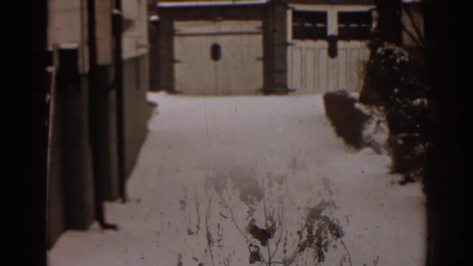 1963 Florida home-movie view of a snow-covered yard or drive facing residential garage doors and side shrubs.