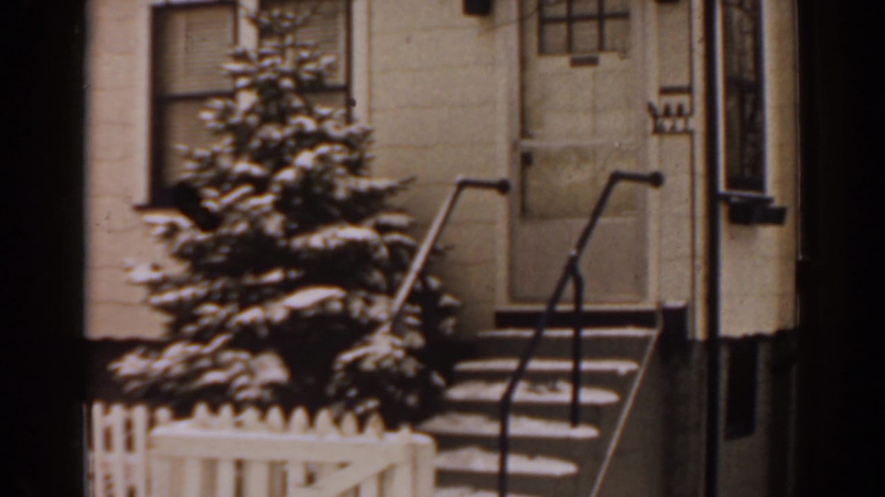 Snow-dusted front yard with evergreen tree, white fence, stoop, and metal railings.