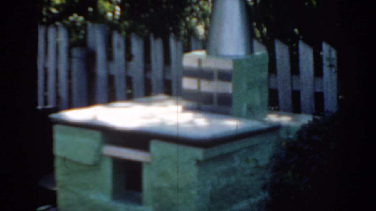 Stone yard structure with flat top, chimney, and fence in background.