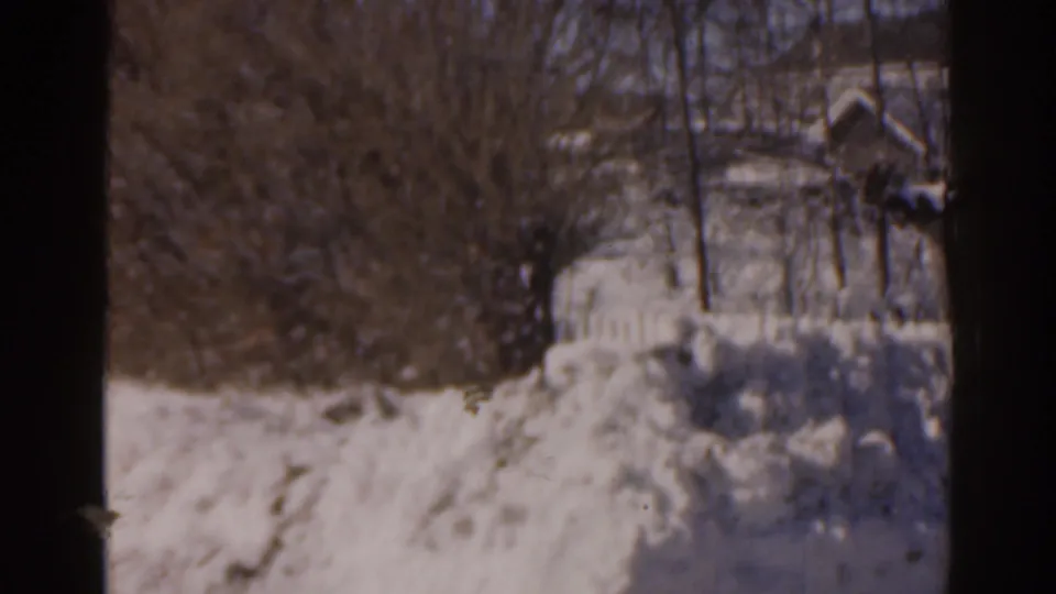 1963 Florida home-movie frame showing deep snow outside a residential window, with bare trees and houses in the background.