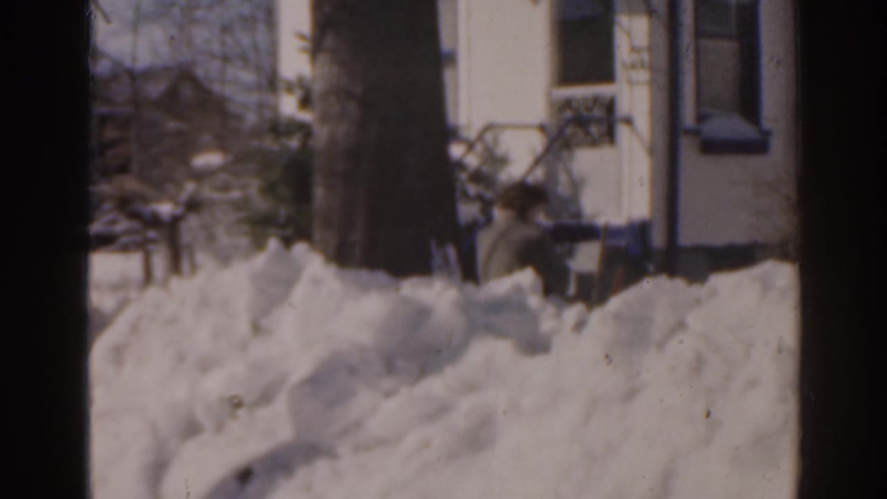 Large snowdrifts beside a house, partly divided by a dark vertical window frame.