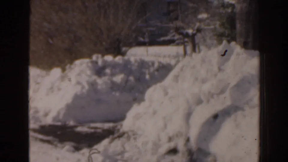 1963 Florida home-movie frame showing a snow-covered yard, distant house shapes, and dark window framing.