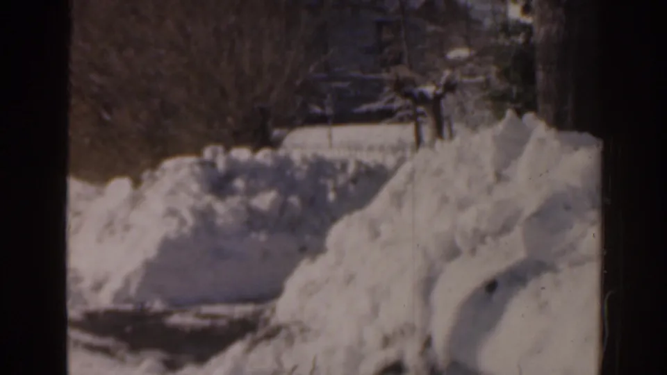 1963 Florida frame showing snowbanks, bare trees, and a distant person near a residential building.